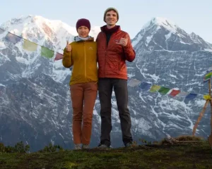a man and woman standing on a hill with a flag in front of mountains